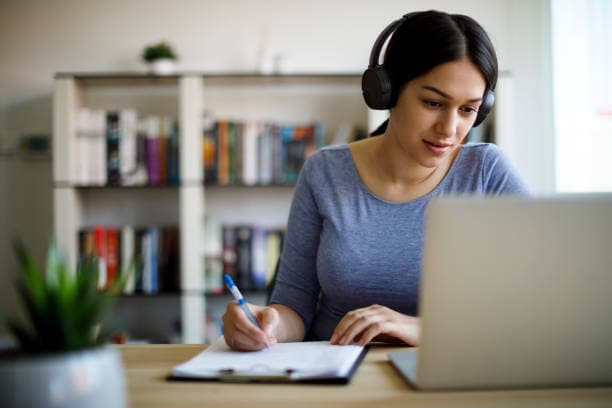 A linguist in headphones taking notes at a desk while preparing for an assignment
